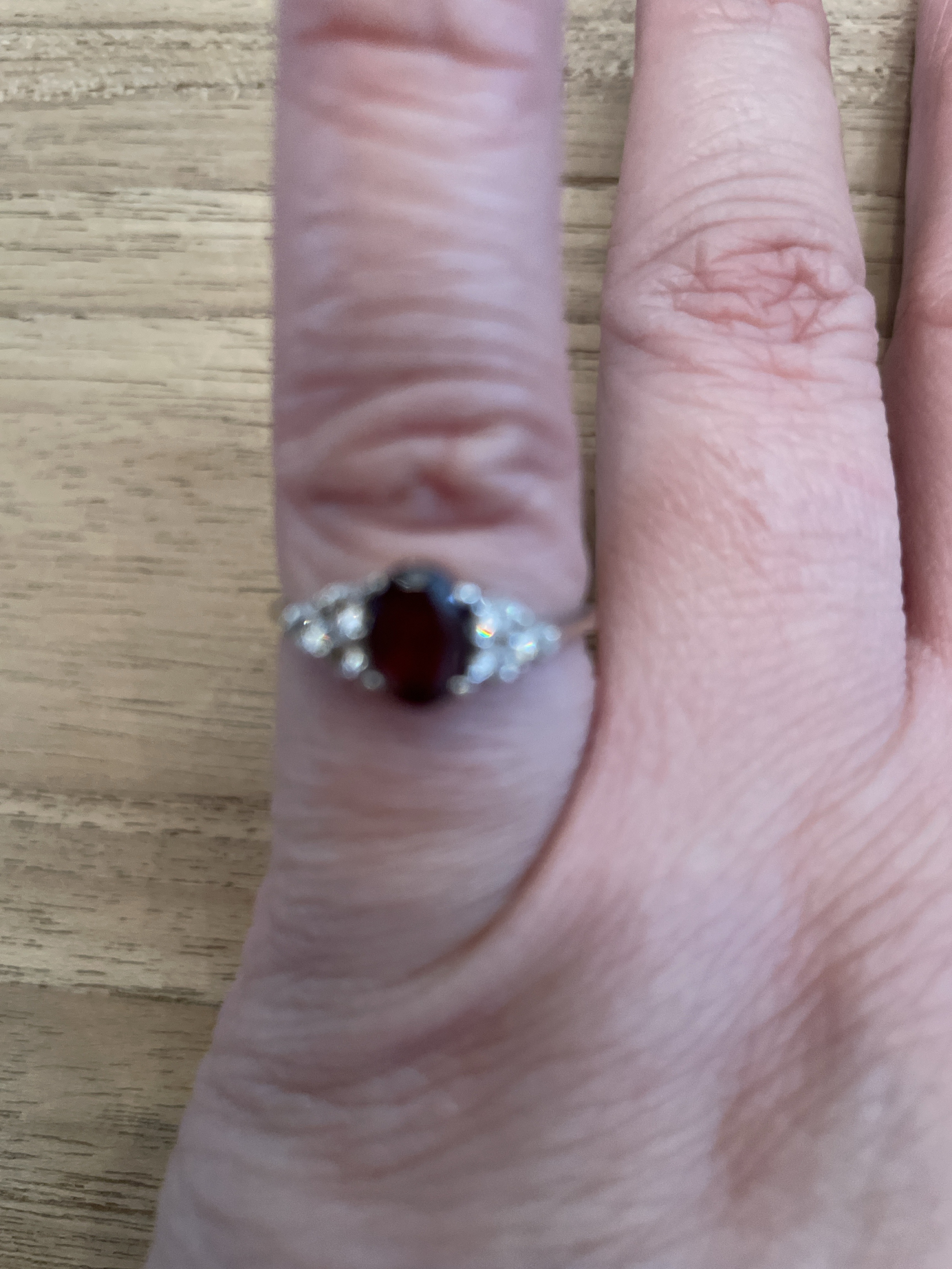 Silberfarbener Ring mit ovalem rotem Mittelstein und seitlichen Akzentsteinen