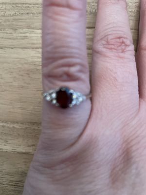 Silberfarbener Ring mit ovalem rotem Mittelstein und seitlichen Akzentsteinen